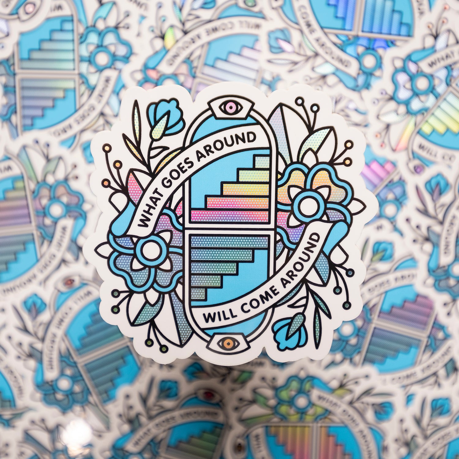 A 3.4x3.3" holographic vinyl art sticker of a symmetrical illustration of opposing arches with staircases that lead up or down surrounds by flowers. Banner are protruding from the arches in a circular composition that read: What goes around will come around. Drawn in a flash tattoo and pop art fusion style in a cyan, white and black color palette by the artist, Red Halftone.